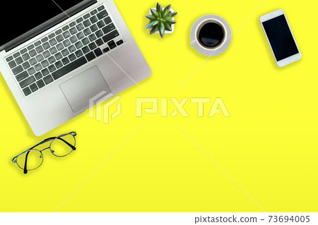 yellow office desk with laptop black coffee cup and glasses Top view with copy area. 73694005