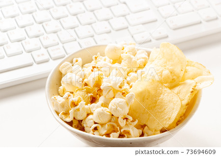 Snack image of online drinking party. Assorted popcorn and potato chips and keyboard. Snack image of online drinking party. Assorted popcorn and potato chips and keyboard. 73694609