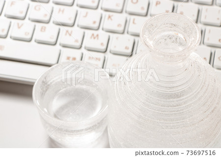 A glass sake set containing sake and a computer keyboard. Online drinking party image. A glass sake set containing sake and a computer keyboard. Online drinking party image. 73697516