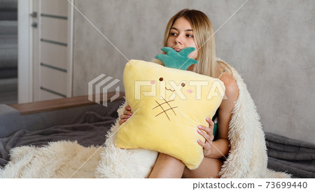 Young woman sitting on sofa and thinking. Beautiful girl holding cushion 73699440