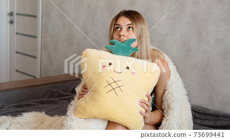 Young woman sitting on sofa and thinking. Beautiful girl holding cushion Young woman sitting on sofa and thinking. Beautiful girl holding cushion 73699441