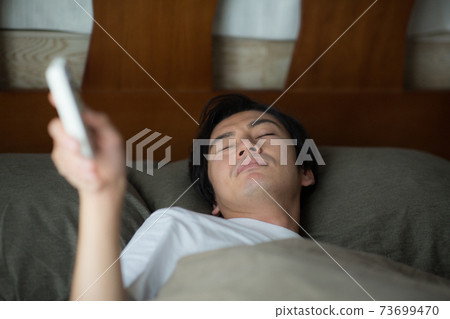 A man operating a remote control from the bed 73699470