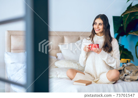 Dark-haired woman with a red cup in her hands looking relaxed Dark-haired woman with a red cup in her hands looking relaxed 73701547
