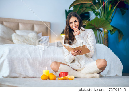Smiling pretty woman siting on the floor and reading a book 73701643