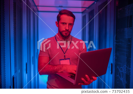Young bearded man with laptop near server Young bearded man with laptop near server 73702435