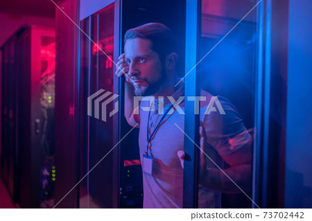 Serious young man peeking out of door 73702442