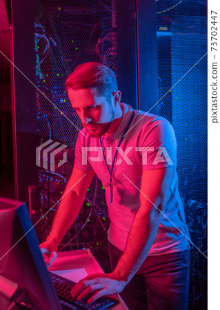 Man staring at computer monitor in data center 73702447