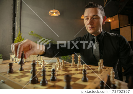 Serious man chess player sitting at home and playing chess alone. 73702597
