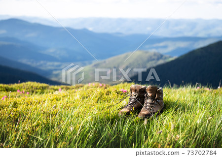 Boots of lonely tourist on lush grass covered mountains hill Boots of lonely tourist on lush grass covered mountains hill 73702784