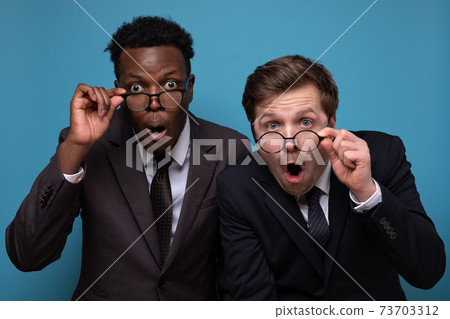Two excited men looking at you wearing glasses being shocked. 73703312