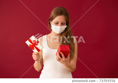 Girl with face mask opening present on valentines day 73703558