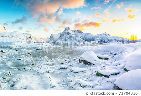 Gorgeous frozen Flakstadpollen and Boosen fjords with cracks on ice during sunrise with Hustinden mountain on background on Flakstadoya island 73704316