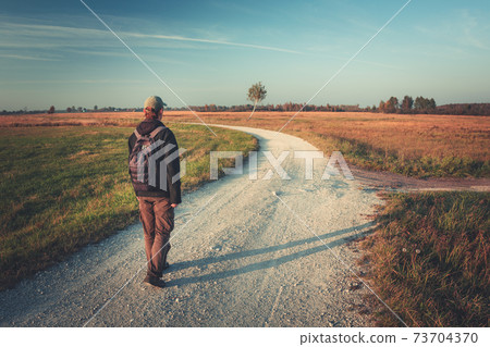 A man with a backpack goes gravel road A man with a backpack goes gravel road 73704370