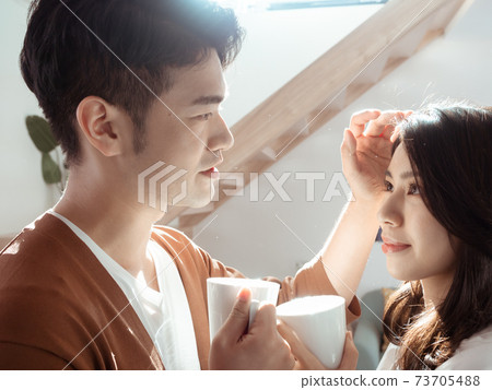 Young asian woman and man are enjoying spending time together at home with cup of coffee in hands. Young asian woman and man are enjoying spending time together at home with cup of coffee in hands. 73705488