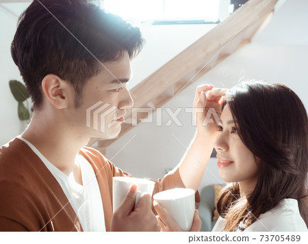Young asian woman and man are enjoying spending time together at home with cup of coffee in hands. Young asian woman and man are enjoying spending time together at home with cup of coffee in hands. 73705489