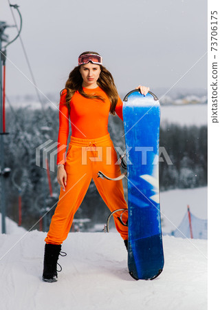 Happy girl snowboarder posing in sunglasses with snowboard 73706175