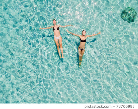 Couple of woman floating in clear blue ocean. Aerial view Couple of woman floating in clear blue ocean. Aerial view 73706995