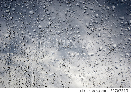 Closeup of rain drops on the window on cloudy sky background Closeup of rain drops on the window on cloudy sky background 73707215