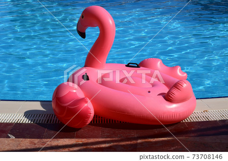 Pink flamingo bird shape inflatable tube near a swimming pool 73708146