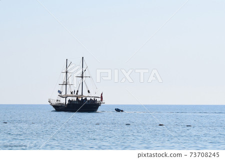 Pleasure craft sailing ship decorated as a pirate, on a background of blue sky and sea 73708245