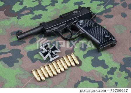 WWII era nazi german army 9 mm semi-automatic pistol with ammunition and Iron Cross award on camouflaged uniform background 73709027