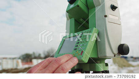 Professional Engineer Surveyor Takes Measures with Theodolite. Worker Using Theodolite Surveying Optical Instrument for Measuring Angles in Horizontal and Vertical Planes on Construction Site 73709192