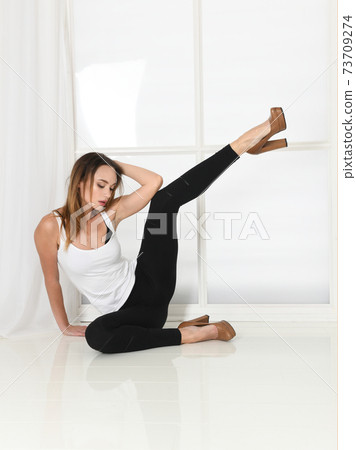 Woman sits in sexy model pose in high heels with leg raised 73709274