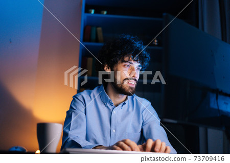 Close-up face of happy smiling bearded young man looking intently at computer monitor screen. 73709416