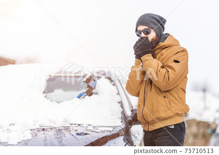 Man clear snow from car with cleaning tool 73710513