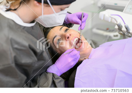 Young female patient visiting dentist office. Beautiful woman sitting at dental chair with open Young female patient visiting dentist office. Beautiful woman sitting at dental chair with open 73710563
