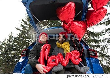 Portrait happy couple faces looking on at each other and laughing. Red heart shape balloons and word love. St Valentines Day celebration, romantic relationships, sincere feelings and love concept 73711469
