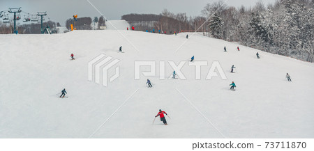View of mountain ski slope with skiers and snowboarders going fast downhill. Alpine skiing and snowboarding. Panoramic view of winter sports nature scenery View of mountain ski slope with skiers and snowboarders going fast downhill. Alpine skiing and snowboarding. Panoramic view of winter sports nature scenery 73711870