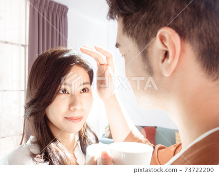 Asian woman and man are enjoying spending time together at home with coffee under sunlight. Asian woman and man are enjoying spending time together at home with coffee under sunlight. 73722200