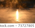 The orange sun shines reflecting off the ice of the river in the winter morning. 73727805