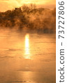 The orange sun shines reflecting off the ice of the river in the winter morning. 73727806