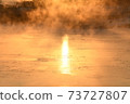 The orange sun shines reflecting off the ice of the river in the winter morning. 73727807
