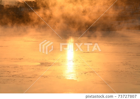 The orange sun shines reflecting off the ice of the river in the winter morning. 73727807
