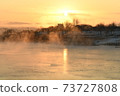 The orange sun shines reflecting off the ice of the river in the winter morning. 73727808