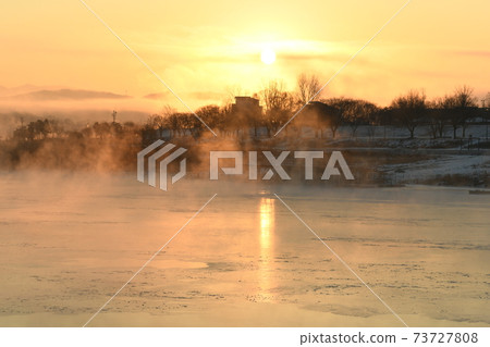 The orange sun shines reflecting off the ice of the river in the winter morning. 73727808