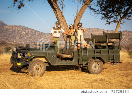 Guide and brunettes in jeep under tree 73729384