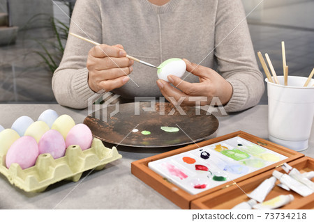Female painting an egg surrounded by eggs and tools 73734218