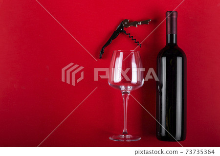 Bottle of red wine and an empty wine glass with a corkscrew next to it. Composition on a red background. Romantic mood. Space for text. Bottle of red wine and an empty wine glass with a corkscrew next to it. Composition on a red background. Romantic mood. Space for text. 73735364