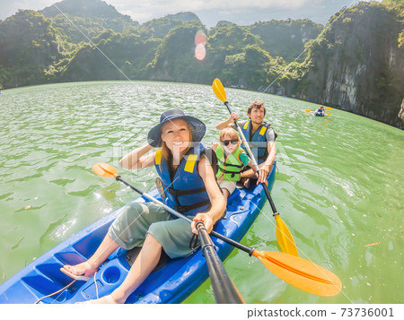 Mom, dad and son travelers rowing on a kayak in Halong Bay. Vietnam. Travel to Asia, happiness emotion, summer holiday concept. Traveling with children concept. After COVID 19. Picturesque sea Mom, dad and son travelers rowing on a kayak in Halong Bay. Vietnam. Travel to Asia, happiness emotion, summer holiday concept. Traveling with children concept. After COVID 19. Picturesque sea 73736001