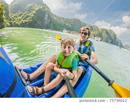 Mom, dad and son travelers rowing on a kayak in Halong Bay. Vietnam. Travel to Asia, happiness emotion, summer holiday concept. Traveling with children concept. After COVID 19. Picturesque sea Mom, dad and son travelers rowing on a kayak in Halong Bay. Vietnam. Travel to Asia, happiness emotion, summer holiday concept. Traveling with children concept. After COVID 19. Picturesque sea 73736022