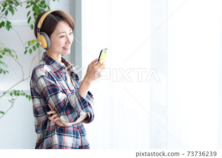 一個女人在室內戴著耳機從智能手機音樂分發應用程序欣賞音樂的女人 一個女人在室內戴著耳機從智能手機音樂分發應用程序欣賞音樂的女人 73736239