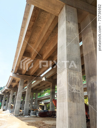 PENANG, MALAYSIA - MARCH 21, 2020: Overhead road under construction. The massive concrete column used to support the concrete road deck. Construction work is in full swing. PENANG, MALAYSIA - MARCH 21, 2020: Overhead road under construction. The massive concrete column used to support the concrete road deck. Construction work is in full swing. 73736982