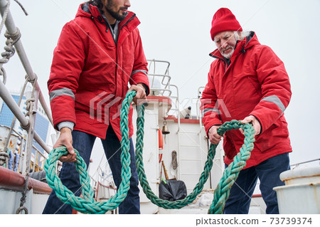 Fisherman and his colleague pulling rope on deck of a boat 73739374