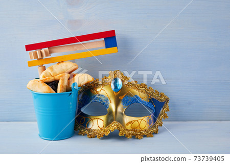 Purim celebration concept with hamantashen cookies, Purim mask and toy noisemaker on blue background Purim celebration concept with hamantashen cookies, Purim mask and toy noisemaker on blue background 73739405