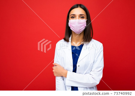 Young beautiful doctor woman in reusable virus protective mask on face against coronavirus isolated 73740992