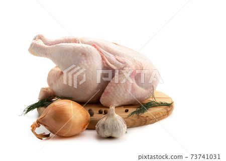 Fresh whole chicken on a cutting board with onions, garlic, pepper and dill. 73741031